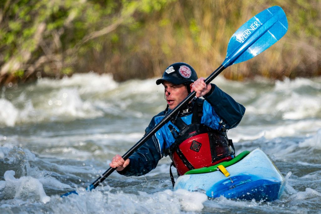 An adventurous kayaker navigates wild rapids in a vibrant blue kayak on a sunny day.